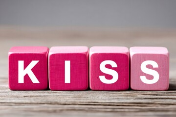 Pink wooden cubes spelling kiss on rustic table