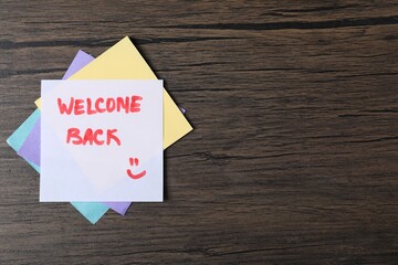 Paper note with phrase Welcome Back on wooden table, top view. Space for text