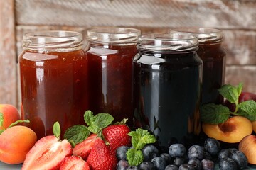 Different jams in jars and ingredients against wooden background, closeup