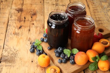 Different jams in jars and ingredients on wooden table. Space for text