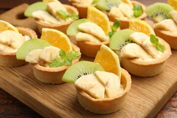 Tartlets with fruits and mint on table, closeup. Delicious dessert