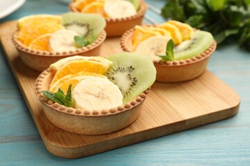 Tartlets with fruits and mint on light blue wooden table, closeup. Delicious dessert