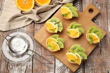 Tartlets with fruits, mint and powdered sugar on wooden table, flat lay. Delicious dessert