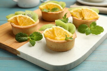 Tartlets with fruits and mint on light blue wooden table, closeup. Delicious dessert