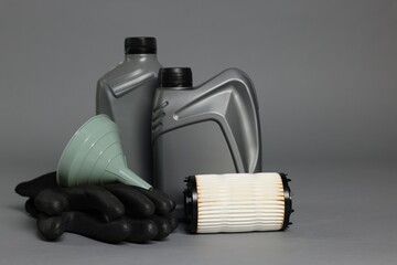 Motor oil in plastic canisters, filter, gloves and funnel on grey background