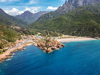 Aerial view of the Genoise tower on a rocky outcrop and the beach at Porto on the west coast of the Mediterranean island of Corsica with mountains behind