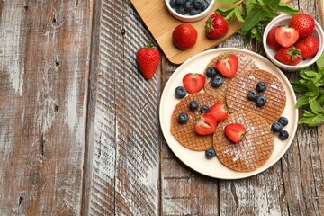 Tasty Dutch waffles (stroopwafels), mint and berries on wooden table, flat lay. Space for text