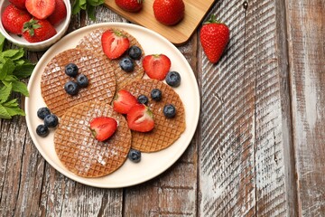 Tasty Dutch waffles (stroopwafels), mint and berries on wooden table, flat lay. Space for text