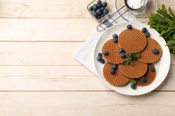 Tasty Dutch waffles (stroopwafels), mint and blueberries on light wooden table, flat lay. Space for text