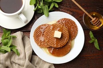 Tasty Dutch waffles (stroopwafels) with honey, butter cube, mint and tea on wooden table, flat lay