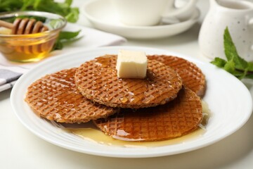 Tasty Dutch waffles (stroopwafels) with honey and butter cube on white table, closeup