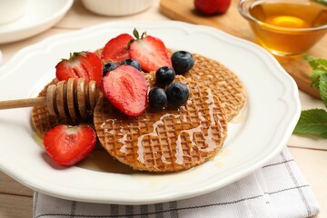 Tasty Dutch waffles (stroopwafels) with honey, strawberries and blueberries on light wooden table, closeup