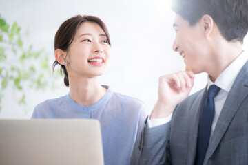 逆光のオフィスでパソコンを見るスーツを着たビジネスマン男女　新人指導やコミュニケーションなどのイメージのクローズアップ