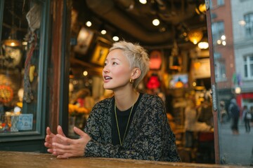 Obraz premium a Asian young woman with short blond hair talking passionately during an interview or conversation. A woman is sitting at a table in a cafe. 