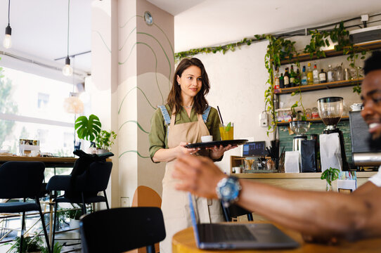Smiling waitress serving coffee to customer while in cafe.