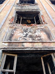 an old structure stands decaying, with peeling paint and shattered windows. atmosphere conveys sense neglect and history in urban setting during daylight. close up.