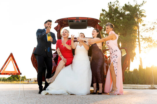 Wedding guests toasting with champagne by car with hazard sign visible
