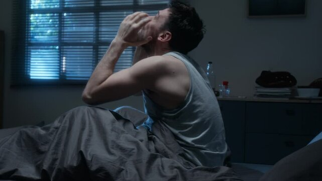 Side view of bearded adult man sitting in bed at night and yelling suffering from insomnia and mental health issues
