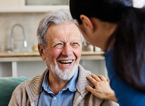 Doctor or nurse caregiver with senior man talking and having fun at home or nursing home