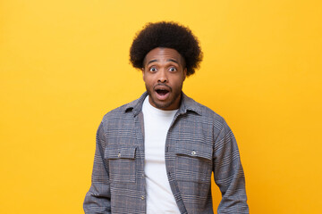 Surprised man looking at camera and reacts with shock on yellow background