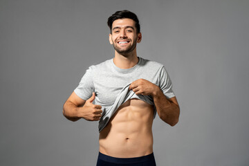 Fit healthy handsome man showing abs and smiling with thumbs up against grey background studio shot