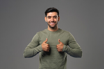 Smiling handsome Caucasian man in casual long sleeve shirt showing double thumbs up on gray background