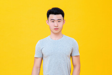 Waist up portrait of casual Asian man in gray t-shirt standing confidently against yellow background
