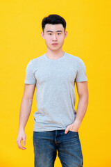 Casual Asian man in grey t-shirt and jeans standing confidently against yellow background