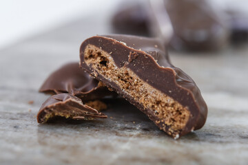 Decadent Chocolate Covered Biscuit Piece, broken in half to clearly show its textured, crumbly interior with hick layer of chocolate coating isolated on marble closeup side view of sweet treat