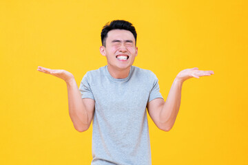 Carefree Asian man smiling with eyes closed and open hands shrugging on yellow background