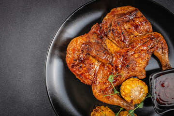 Whole grilled chicken glazed with barbecue sauce served on a black plate with corn cobs and a side of dark dipping sauce