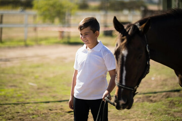 Boy holding dark brown horse by lead rope in paddock with wooden fence rails, copy space