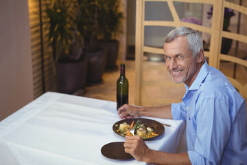 Senior man holding fork and knife at restaurant table with plated meal and wine, copy space © wavebreak3