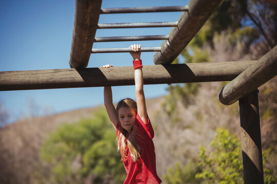 Child girl hanging by arms on wooden monkey bars at park wearing red t-shirt wristband - Powered by Adobe