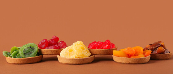 Bowls with different candied fruits on brown background