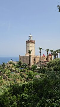 Scenic view of Cap Spartel's lighthouse in front of the ocean surrounded by greenery on a sunny day - Tangier, Morocco 