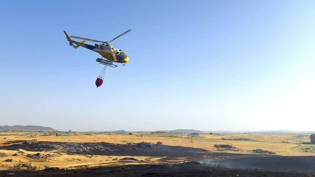 Helic&oacute;ptero apagando incendio con bambi descargando agua en vuelo
