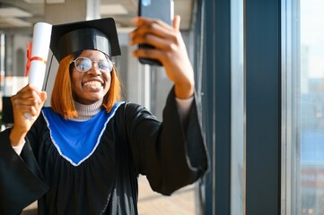 education, graduation, technology and people concept. An African girl, a university graduate, takes...