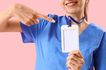 Female medical intern pointing at badge on pink background, closeup
