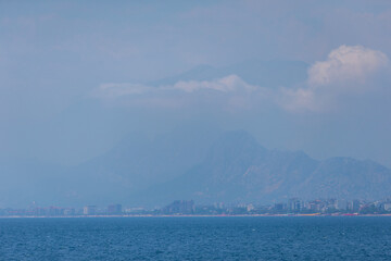 A landscape with a blue sea and a city blurred in the distance near a mountain.