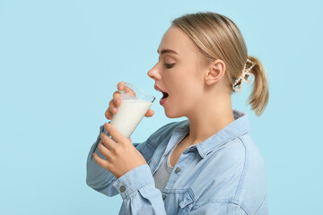 Pretty young woman drinking milk on blue background