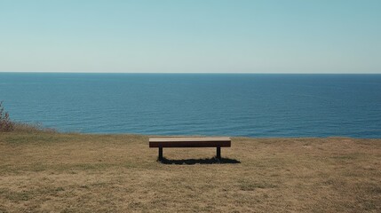 A solitary wooden bench sits on a grassy cliff overlooking a calm, expansive ocean under a clear blue sky