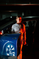 Woman exits blue car at night with a flashlight in a dimly lit parking area