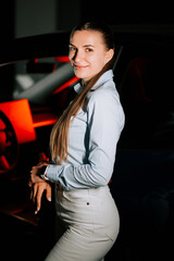 Woman in light blue shirt posing confidently near a car during evening setting