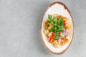 A marinated mushroom salad with red onion rings, chili pepper slices, parsley, and a light dressing served in an elegant oval dish on a gray background