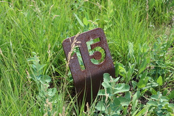 close-up rusty steel iron signpost marker depicting 15 in rich green grass in bright summer sunshine