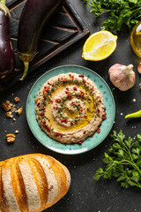 Plate of tasty baba ghanoush with ingredients on black background