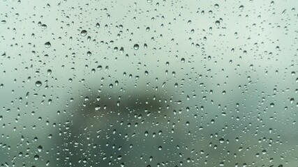 Close-up view of raindrops on a glass window during a rainy day, with a soft, blurry background creating a calm and moody atmosphere.
