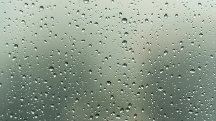 Close-up view of raindrops on a glass window during a rainy day, with a soft, blurry background creating a calm and moody atmosphere.