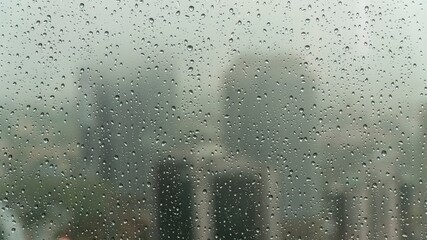 Close-up view of raindrops on a glass window during a rainy day, with a soft, blurry background creating a calm and moody atmosphere.